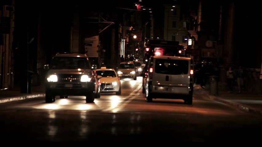 Street-level night footage of a Roman intersection full of cars, buses, and