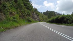 Video footage of high stone slopes with green vegetation on roadside during automobile move on paved highway.View of trucks and cars riding on autostrada 