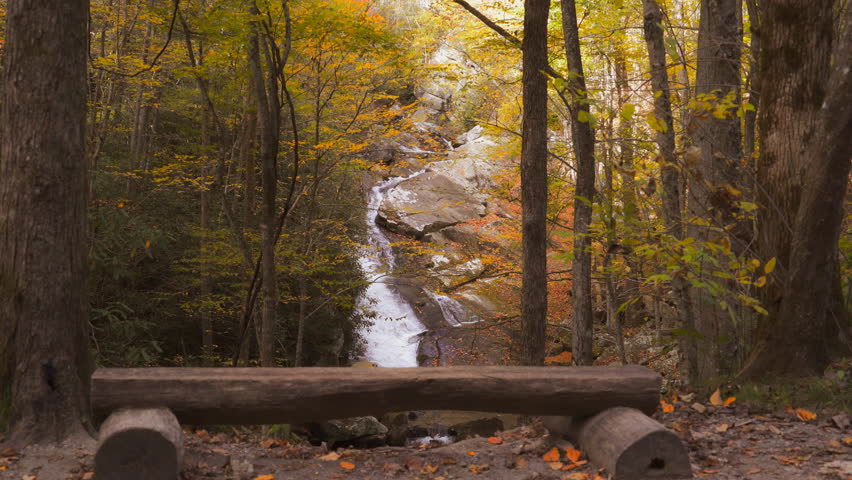 A rustic bench overlooks a water fall surrounded by colorful autumn trees in the Appalachian mountains of Tennessee