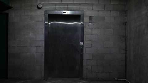 An Elevator door opens in the basement ground level of dark parking garage ALT