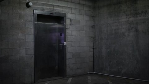 An Elevator door opens in the basement ground level of dark parking garage