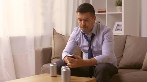 alcoholism, alcohol addiction and people concept - male alcoholic with smartphone drinking canned beer or cocktail and talking to himself at home