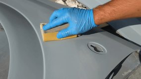 Manual cleaning of a car part for further painting. In the video, a hand in a blue glove with a special roller and grater cleans and smoothes the surface for painting.