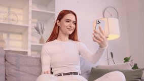 Portrait of beautiful young woman having video call conference meeting by smartphone sitting on couch at home Smiling confident female talking on working or personal conversation indoors