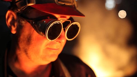 Hard work in the foundry, worker watching and controlling iron smelting in furnaces, too hot and he putting protective eyewear