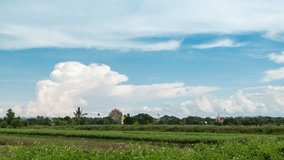Blue sky with white clouds moving and rolling over the vegetable plot and temple (public place) in Thailand. 4k time lapse footage.