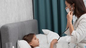 Doctor woman in white coat listening sick child girl with stethoscope sitting on bed. Pediatrician woman with stethoscope checking little patient girl