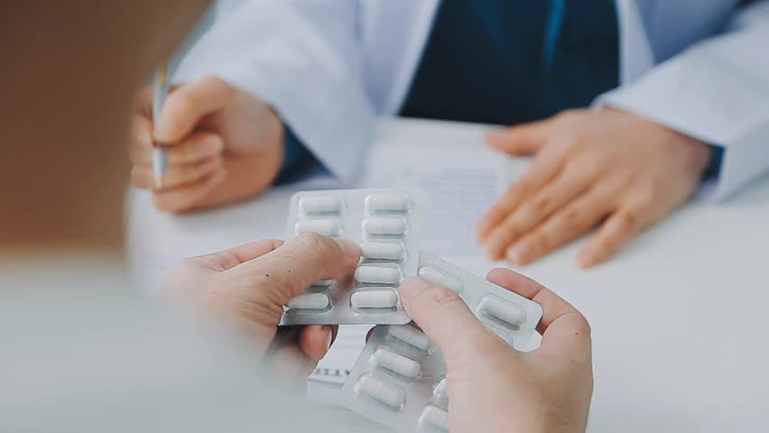 Asian caregiver nurse give consult to Caucasian senior woman patient. Attractive carer pharmacist hold medicine pills bottle, explain prescription to elderly mature grandmother in living room in house