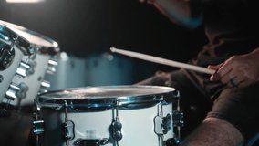 The drummer plays drums in a dark studio with lights on the back. Slow motion video.