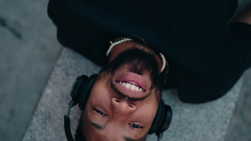 Top view, relaxed music lover with closed eyes lying back in urban setting while streaming a new album release and appreciating every beat with high-quality sound in noice cancelation headphones