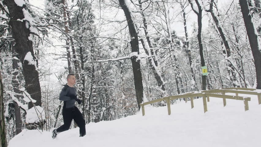 Slow Motion Of Muscular Sportsman Jogging Outdoors Through Snow