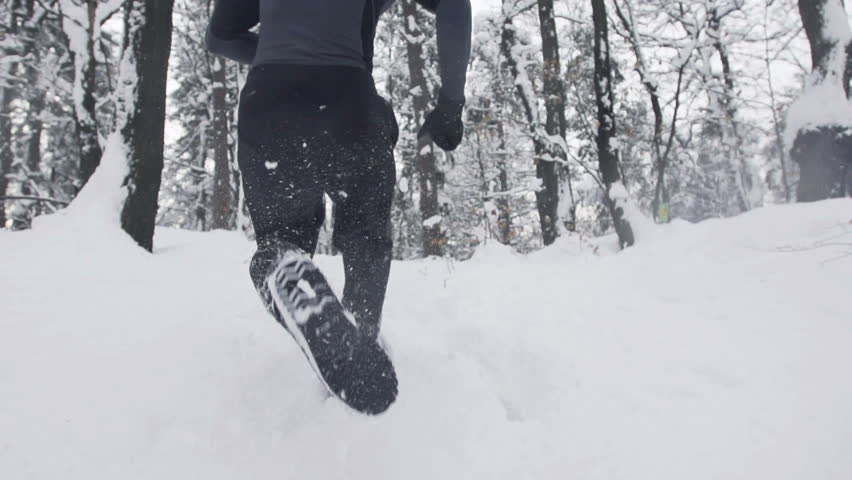 Slow Motion Of Young Sportsman Running Through Snowy Forrest. Shot In The Back.