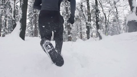 Slow Motion Of Young Sportsman Running Through Snowy Forrest. Shot In The Back. : vidéo de stock