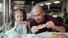 Dad with a little daughter enjoying the taste of fragrant pizza in a pizzeria