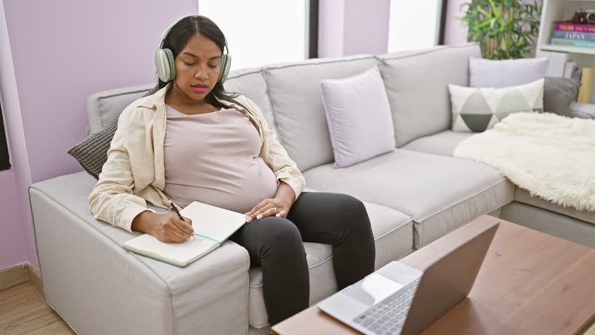 Expecting young hispanic woman working from home, sitting on sofa, studying maternity documents, taking notes while telecommuting via video call Royalty-Free Stock Footage #3387449395