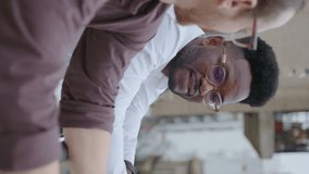 Young Black businessman having a talk with colleague on urban rooftop, spending a break together outside during workday. Vertical format video, rack focus