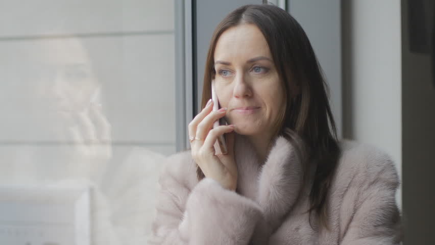 Girl in bright coat talking on a cell phone at the window | Shutterstock HD Video #33878284