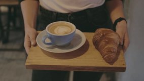 Camera follows waiter who carries tray or wooden artisan board with freshly baked croissant and specialty coffee at downtown cafe or shop. Concept hospitality or restaurant business