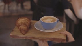 Camera follows waiter who carries tray or wooden artisan board with freshly baked croissant and specialty coffee at downtown cafe or shop. Concept hospitality or restaurant business