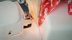Female designer works on sewing machine. Woman's hands sew fashion clothes, close up. Creation and tailoring clothes. Details of overlock machine. Vertical video