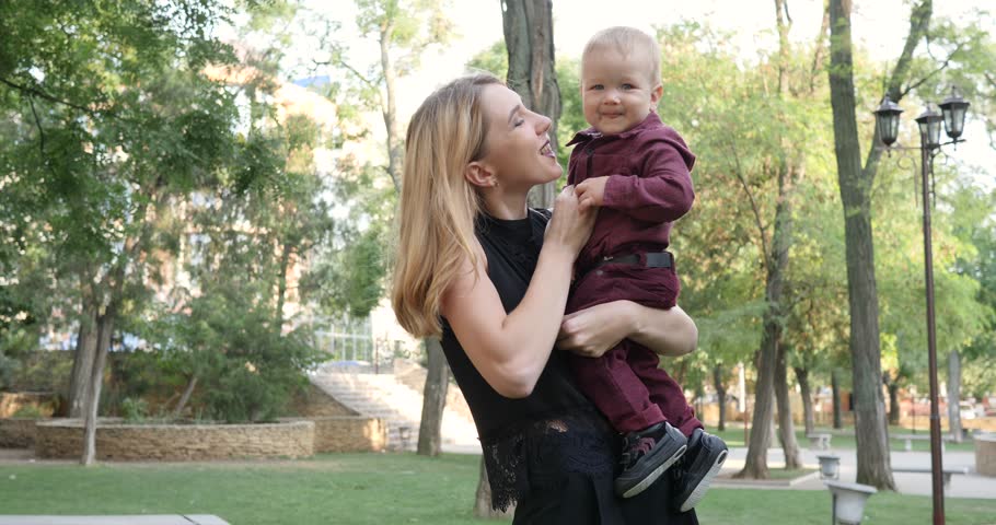 mum tickles and playing with her son, baby laughing in hands of mother on background park