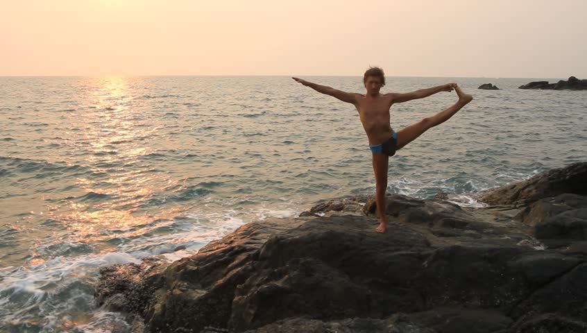 Young man doing yoga exercise on the deserted wild stone sea beach (HD) 