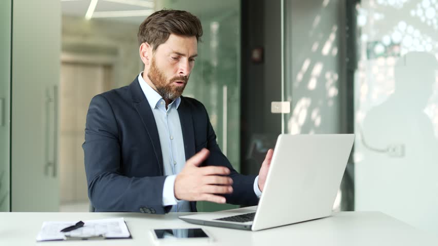 Frustrated businessman in a formal suit having problems with software or service on laptop computer sitting in business office. Worried disappointed worker complains about a bad internet connection | Shutterstock HD Video #3389378251