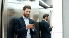 Businessman in formal suit is using smartphone while standing in the elevator in a modern office building. Worker reads or types message, chats, browses social networks, checks email or swiping online - Powered by Shutterstock - Get 15% off with code: PIKWIZARD15