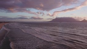 4K high quality aerial video view of Western Cape's coast, Bloubergstrand sandy beach, sea birds flying around and view of Table Mountain in the background in Cape Town, South Africa on summer evening