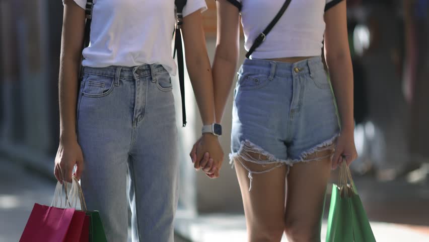 Young female friends holding shopping bags are walking on the sidewalk in Bangkok, Thailand.
