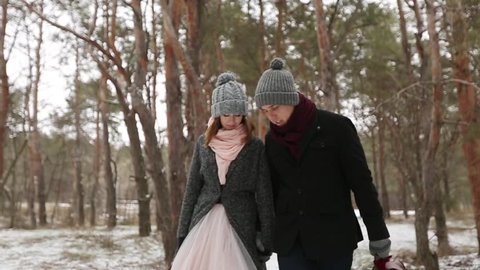 Outdoor winter forest shot of young wedding couple walking and having fun holding hands in snow weather pine forest during snowfall. Snowy engagement ceremony.