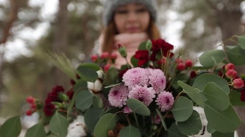 Portrait of beautiful mixed race caucasial asian girl holding a bouquet of flowers in winter snowy pine forest during snowfall and waiting for groom and first meet. Valentines Day concept.