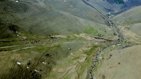 Aerial view of the valley of a winding small mountain river. Snow thawed along the banks, trees without leaves, small old houses. Deserted gray mountains in winter without grass. Drone footage Armenia