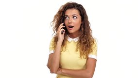 Happy pretty curly woman in dress talking by smartphone and looking at the camera over white background