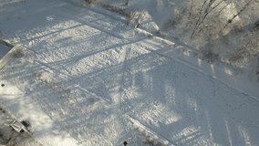 An unidentified hiker strolls through a winter park adorned with snow-covered trees. Beautiful snowy landscape in the park, captured from an aerial perspective. accelerated video