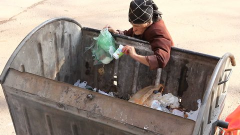 Woman in urban poverty. Homeless woman is searching for food in garbage dumpster. Woman in poverty is searching something in container.
