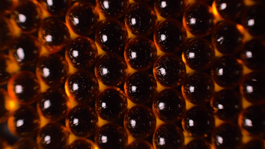 Broun transparent capsules of fish oil are lined up in a row. Macro. Closeup. Dolly shot. Bottom view