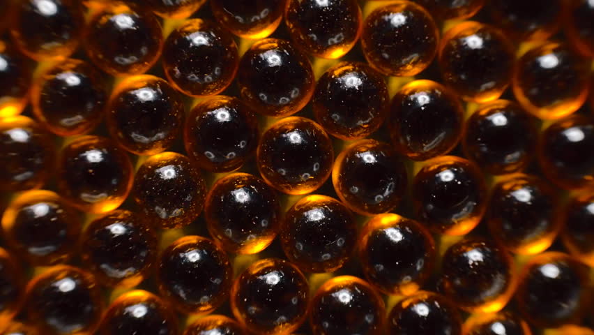 Broun transparent capsules of fish oil are lined up in a row and rotation. Macro. Closeup. Dolly shot. Bottom view