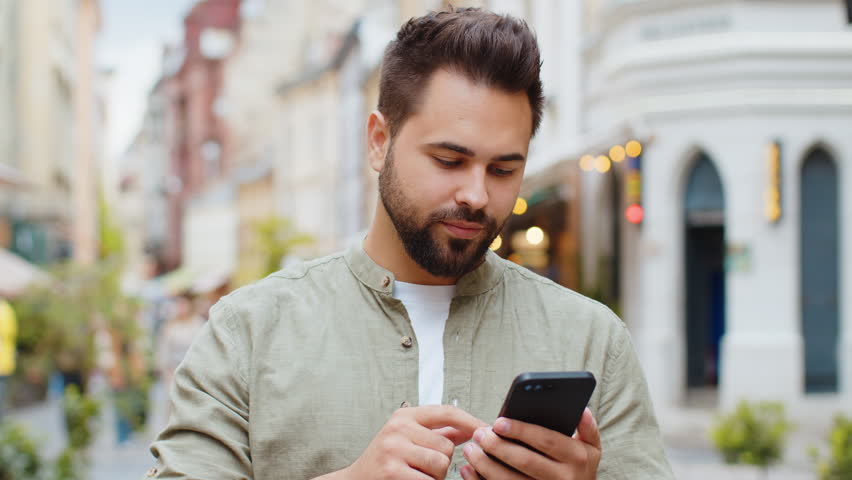 Caucasian bearded man use smartphone typing browsing, loses becoming surprised sudden lottery results, bad news, fortune loss, fail. Young guy walking in urban city street outdoors. Town lifestyles Royalty-Free Stock Footage #3390195865