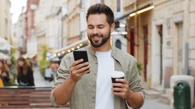 Happy smiling man use smartphone typing text messages browsing internet social media web app working chatting online enjoying morning to-go coffee hot drink outdoor. Guy tourist walking in city street - Powered by Shutterstock - Get 15% off with code: PIKWIZARD15