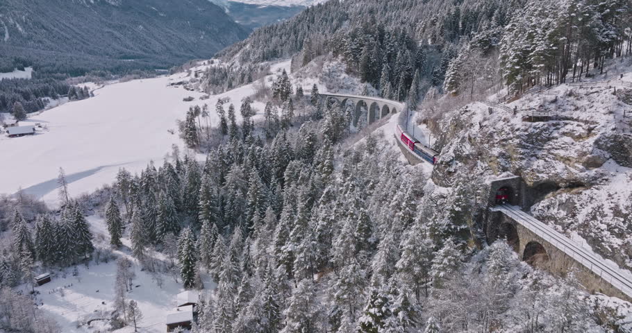Landwasser Viaduct world heritage sight with luxury Glacier and Bernina express in Swiss Alps snow winter scenery. Aerial Drone shot red train passing through famous mountain in Filisur, Switzerland.