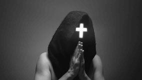 A man with neon cross on his face covered with black mask praying