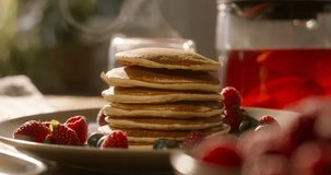 Perfectly arranged pancakes with raspberry over them, in slow motion, hot tea background. No people, advertising, cinematic. Home cooking, individual approach to each client. Guilt-free cheat meal