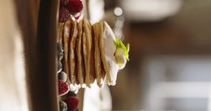 Side view of pancakes with berries, syrup and sugar powder in kitchen, slow motion. Lifestyle, food, cooking and domestic life. Vertical video. Beautiful cinematic video for social networks aesthetics