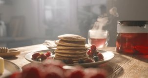 Pancakes with berries, syrup, and sugar powder in kitchen. No people, advertisement. Stunning perfect pancakes stuffed with berries dusted with powdered sugar. Pleasant family traditions. Cheat meal