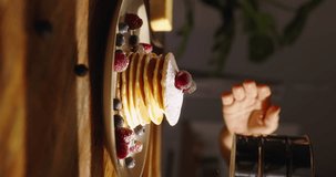 Unrecognizable woman sprinkling sugar powder onto mouthwatering stack of pancakes. Lifestyle, food, cooking and domestic life. Advertising vertical beautiful aesthetics cinematic video, social media 