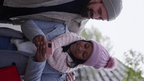Vertical video. young couple interracial in love using mobile phone enjoying winter holiday season in the city streets, walking and hugging and holding gift bags while celebrating Christmas outdoors - Powered by Shutterstock - Get 15% off with code: PIKWIZARD15