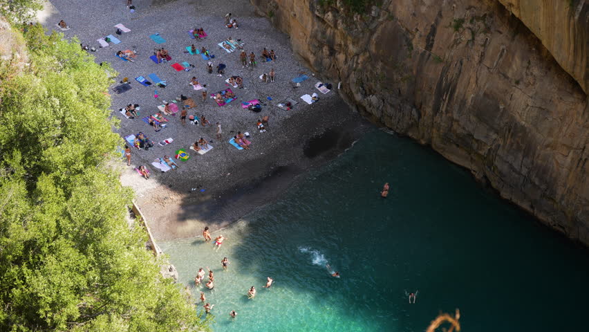 Top view from Fjord Furore Bridge to people relaxing and swimming on beach in Amalfi Coast on summer sunny day. Scenic vacation destination for tourists on Amalfi Coast in Italy, slow motion.