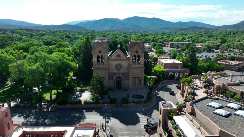 Cathedral Basilica of St. Francis of Assisi in Santa Fe, New Mexico. Historic stone church with twin bell towers in lush mountain scenery. Aerial.