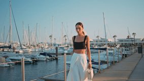 Calm woman walking port in trendy outfit. Elegant carefree female tourist strolling at embankment with luxury yachts. Confident posh girl going at beautiful ocean pier. Chic lady model enjoy promenade - Powered by Shutterstock - Get 15% off with code: PIKWIZARD15
